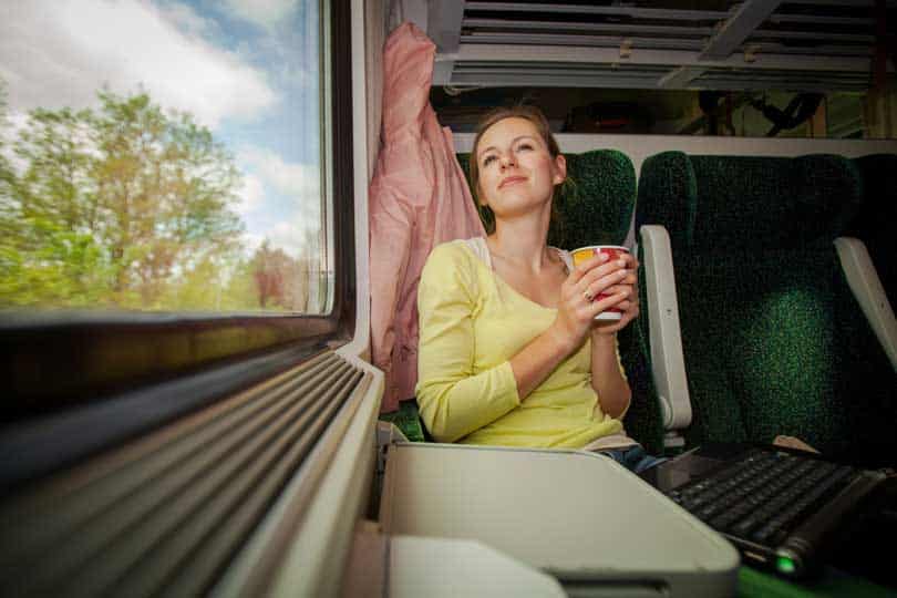 Woman sat on Irish Rail train holding a drink smiling, sat next to a window